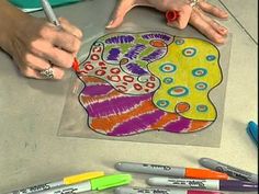 two hands are drawing on a piece of paper with markers and crayon pens