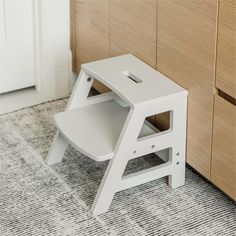 a white step stool sitting on top of a carpeted floor next to a wooden cabinet