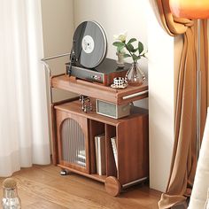 a record player sitting on top of a wooden table next to a window with curtains