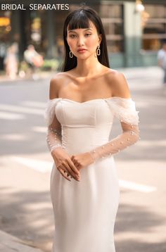 a woman in a white dress is standing on the street with her hands behind her back