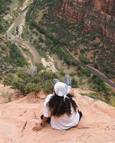 a woman sitting on top of a cliff with her head in the air and looking down