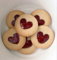 four heart shaped cookies in a bowl with jelly on top and one cookie has been cut into the shape of a heart