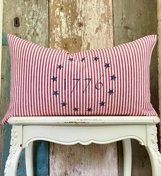 a red and white striped pillow sitting on top of a wooden bench next to a wall