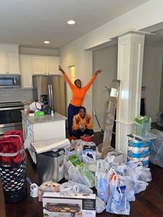 two people standing in the middle of a kitchen surrounded by plastic bags and other items