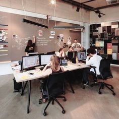 a group of people sitting at desks in an office with computers on the wall