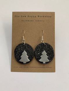 the black and silver earrings are decorated with a small white christmas tree on it's side