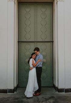 a man and woman standing in front of a green door with their arms around each other