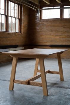 a wooden table in an empty room with brick walls and windows on either side of it