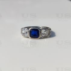 a ring with a blue stone surrounded by three diamonds on a white surface, close up