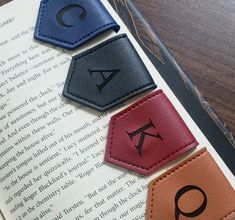 three leather bookmarks with letters and symbols on them sitting on top of an open book