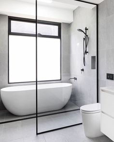 a white bath tub sitting next to a toilet under a window in a gray bathroom