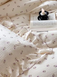 an open book on a bed with white sheets and purple flowered bedspread