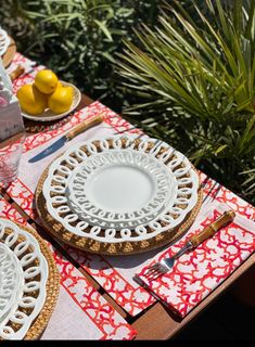 the table is set with plates, silverware and lemons on red napkins