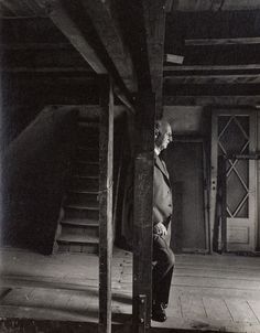 an old photo of a man leaning against a pillar in the middle of a room