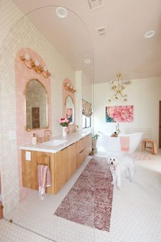 a white dog standing in a bathroom next to a bath tub and sink with mirrors on the wall