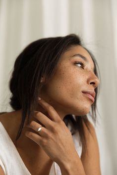 a woman with freckled hair is wearing a white shirt and holding her hand on her neck