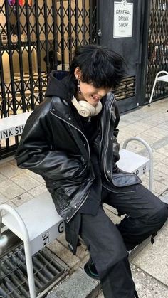 a man sitting on a bench with headphones in his ears and wearing black leather jacket