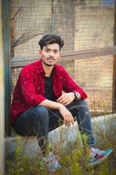 a young man sitting on the ground in front of a fence with his hands crossed