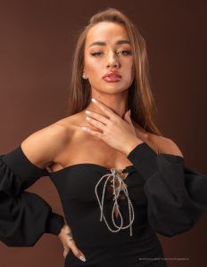 a woman posing with her hands on her chest and wearing an off the shoulder black dress