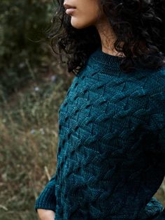 a woman with curly hair wearing a green knitted sweater in the woods looking off into the distance