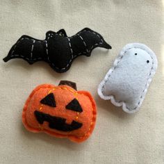 three felt halloween decorations are laying on a white cloth surface, one has a bat and the other is a pumpkin