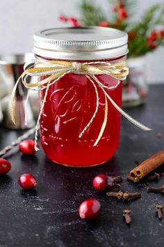 a glass jar filled with red liquid surrounded by cinnamons and cloves on a table