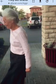 an old woman walking down the street with her hand in her hair and wearing a white sweater