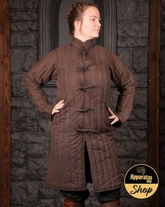 A knee-length, lightly padded coat with straight quilting. The flat fasteners make it ideal as a layer of padding under a chainmail shirt or a cuirass. The stand-up collar also provides optimal protection for the neck from pressure points. Thanks to the long sleeves, you can use either a long-sleeved chainmail shirt or one with short sleeves and bracers. The sleeves are set relatively far in at the front, which makes them particularly flexible. A useful companion for a wide variety of fighting c Medieval Fitted Winter Outerwear, Medieval Long Sleeve Winter Outerwear, Medieval Long Coat For Winter, Medieval Style Long Winter Coat, Medieval Style Brown Winter Outerwear, Chainmail Shirt, Padded Coat, Pressure Points, Chain Mail