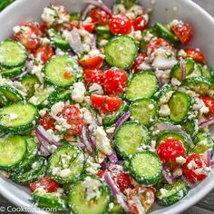 a bowl filled with cucumbers, tomatoes and other vegetables on top of a wooden table