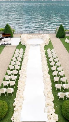 an outdoor ceremony setup with white chairs and flowers on the grass by the water's edge