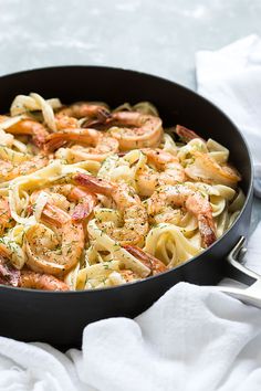 a skillet filled with shrimp and pasta on top of a white towel next to a fork