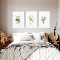 a bed with white sheets and pillows in a bedroom next to two pictures on the wall