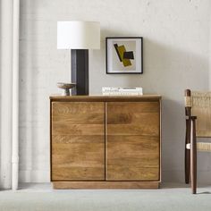 a wooden sideboard sitting next to a lamp on a white wall in a living room