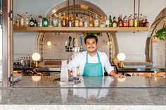 a man standing behind a bar with lots of bottles on the wall and shelves above him