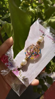 a person holding up a small glass bead with flowers on it in front of some leaves