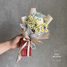 a hand holding a bouquet of daisies and baby's breath with a tag