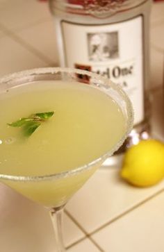 a drink in a glass with a green leaf on the rim and a bottle next to it