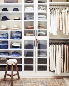 an organized closet with clothes and hats on the shelves in front of it, along with a stool