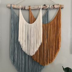 the wall hanging is decorated with two different colors of yarn and wood, along with a branch