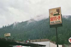 a sign for drive - in inside seating with mountains in the background