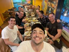 a group of men sitting at a table with food in front of them and smiling for the camera