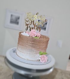 a three tiered cake with pink flowers on the side and gold glitter topper