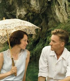 a man and woman sitting next to each other under an umbrella in front of a waterfall