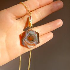 a woman's hand holding a necklace with an agate pendant