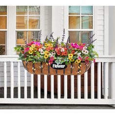 a flower pot hanging from the side of a white porch with flowers growing in it