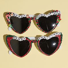 two heart shaped sunglasses with merry christmas decorations on the top and bottom one is black