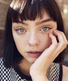 a woman with freckled hair and blue eyes poses for the camera while holding her hand to her face