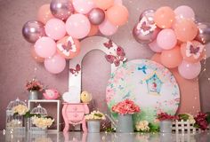 a table topped with lots of balloons next to a wall covered in pink and white flowers