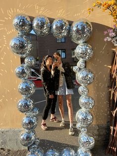 two women are taking a selfie in front of a mirror ball sculpture on the sidewalk