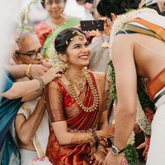 a woman in a red and gold sari smiles as she is surrounded by other people